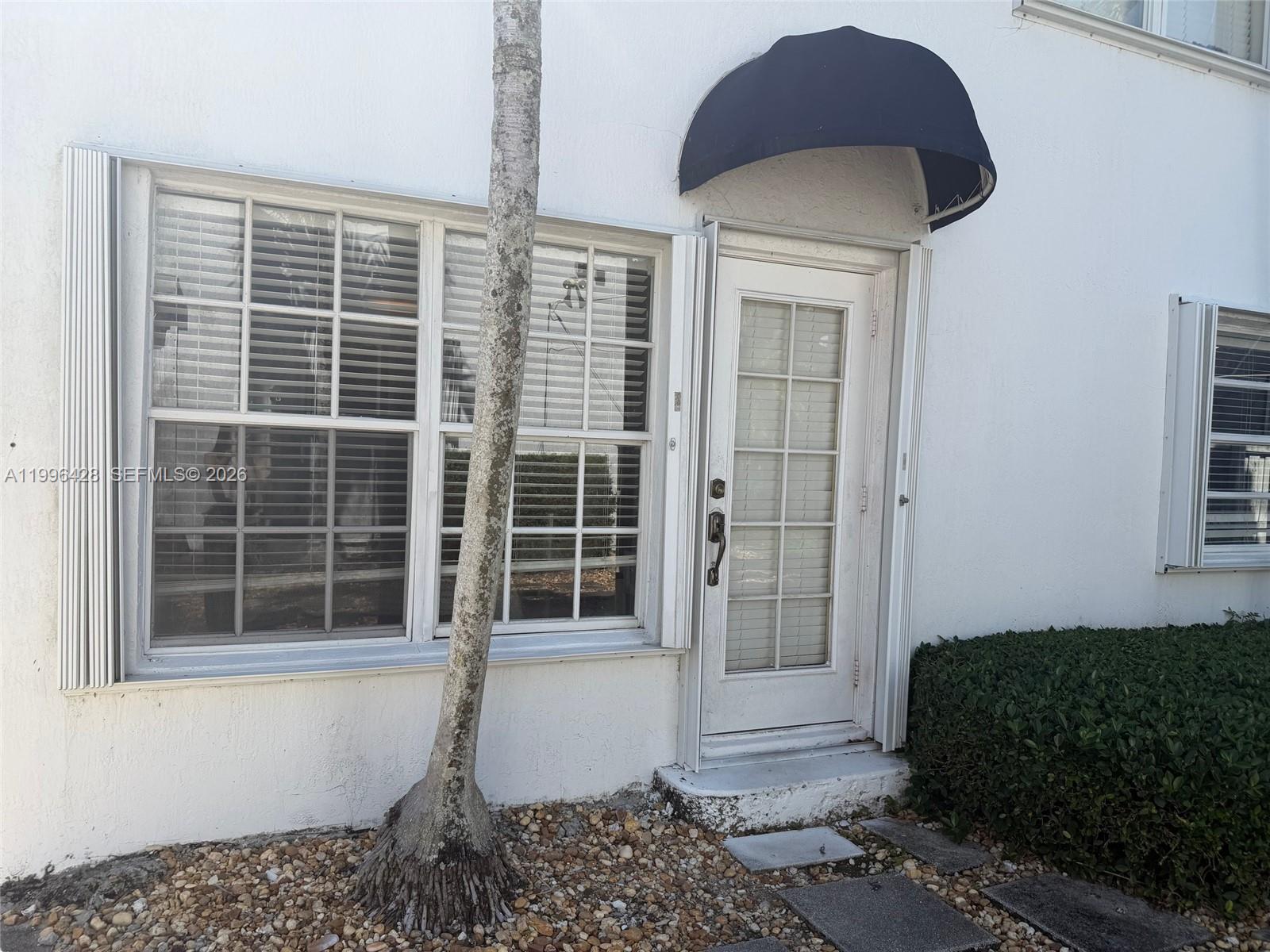 A white exterior wall features a large window, a glass-paneled door, and a dark awning — 5116 SW 57th Ave # A, Miami FL 33155, MIAMI, FL
