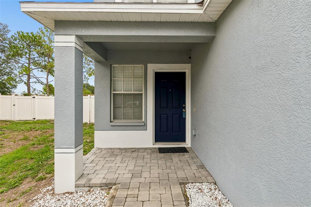 A gray house exterior features a covered entryway with a paver porch and blue door — 12610 ADVENTURE DRIVE, RIVERVIEW, FL
