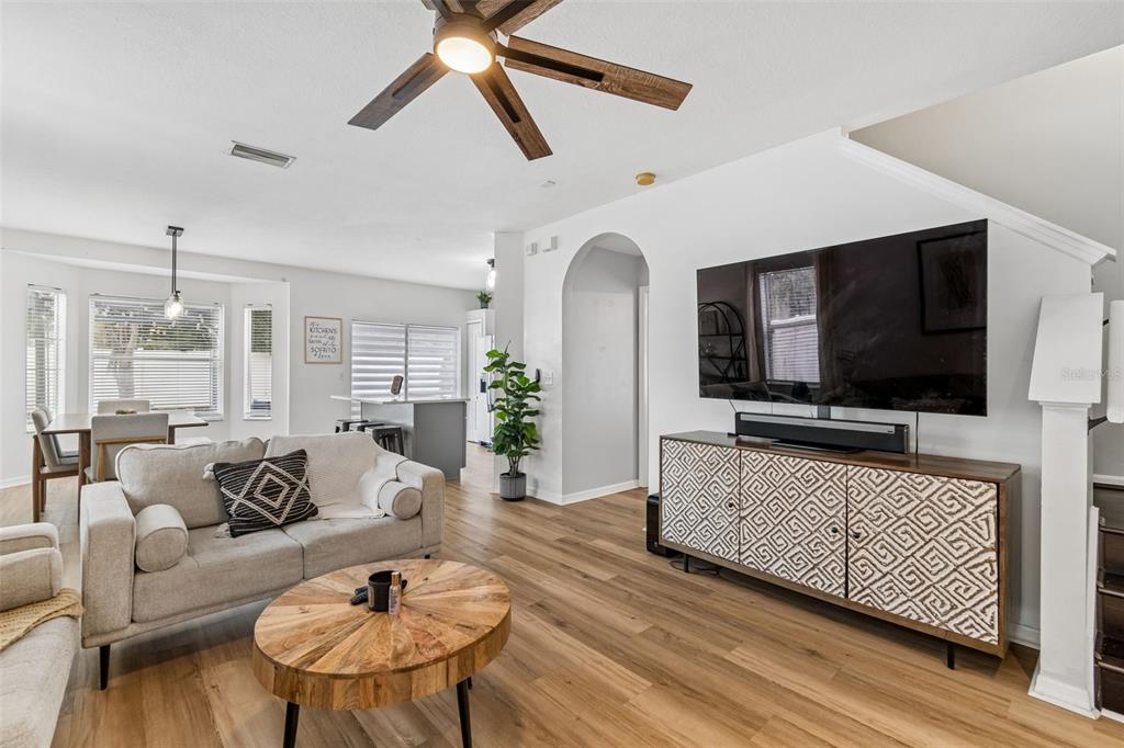 A living room features light wood flooring, a patterned media console, and a ceiling fan — 12610 ADVENTURE DRIVE, RIVERVIEW, FL