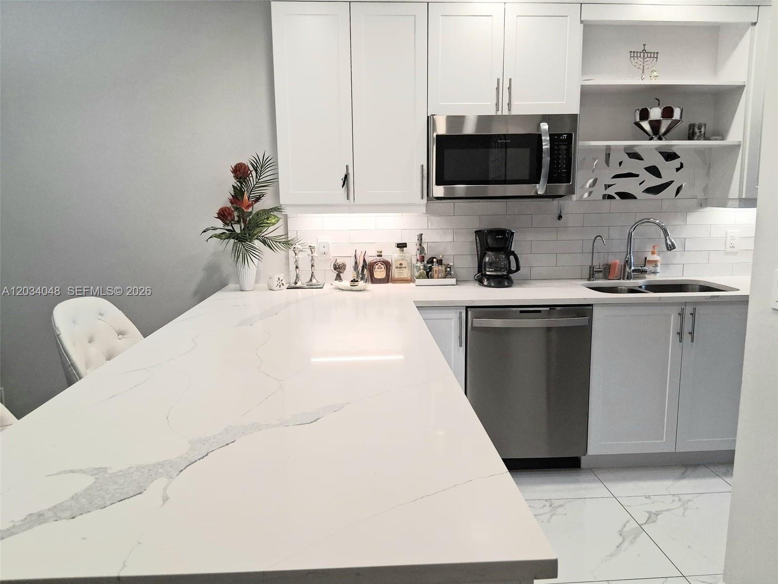 A modern kitchen features white cabinets, quartz countertops, stainless steel appliances, and white tile flooring — 1150 Boxwood Dr # 101, Delray Beach FL 33445, DELRAY BEACH, FL