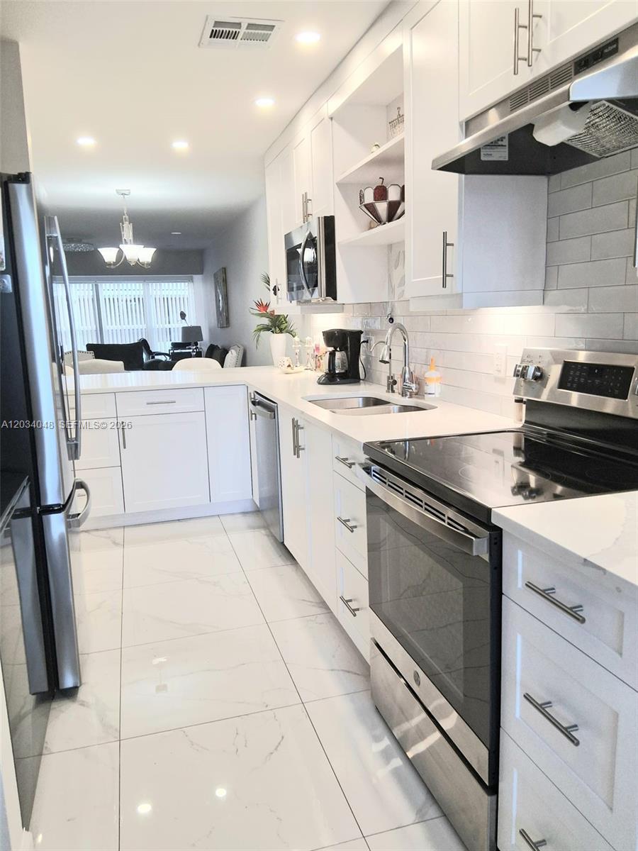 A modern kitchen features white cabinets, stainless steel appliances, and white tile flooring — 1150 Boxwood Dr # 101, Delray Beach FL 33445, DELRAY BEACH, FL