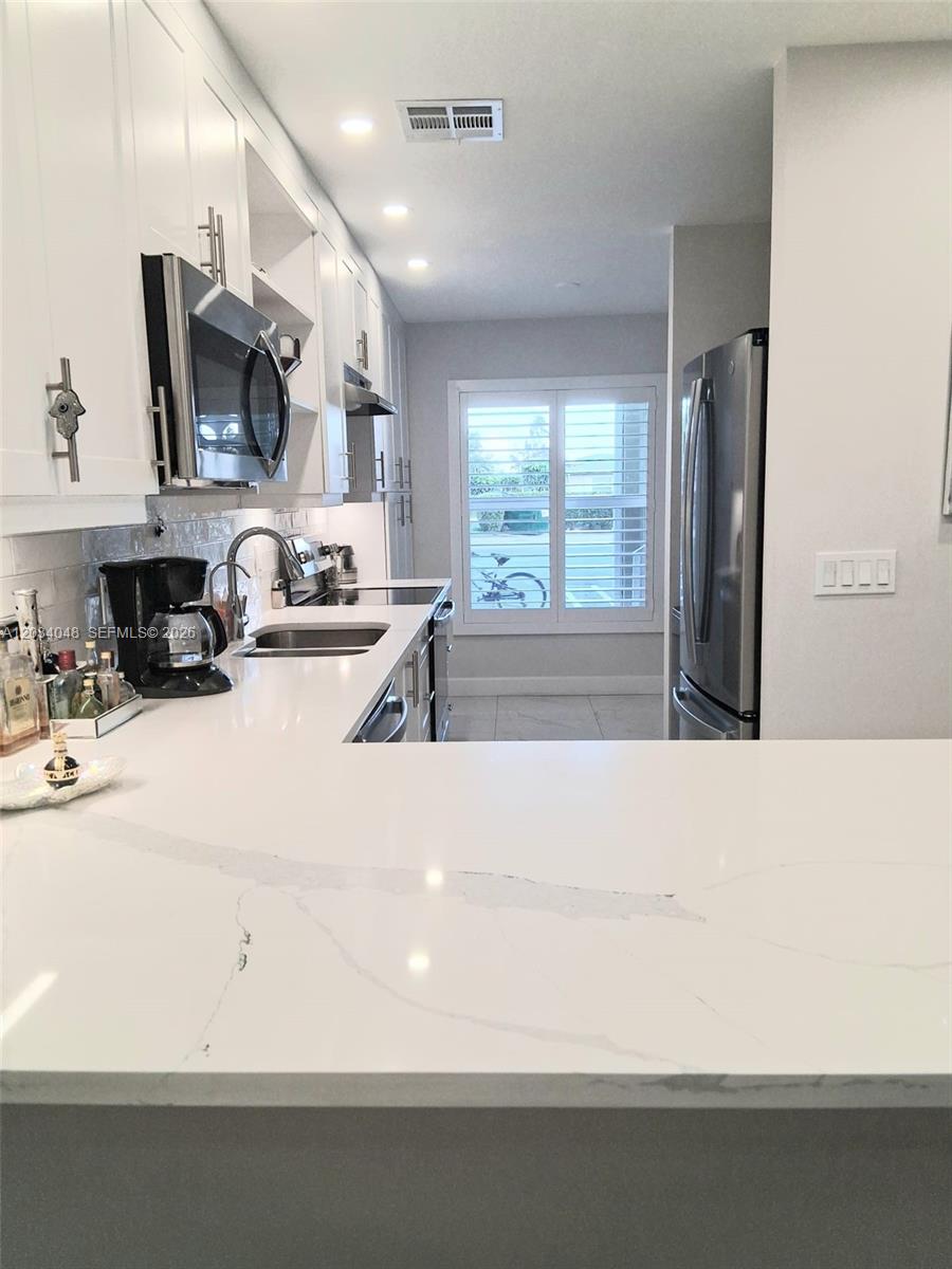 A modern kitchen features white cabinetry, stainless steel appliances, and a white quartz countertop — 1150 Boxwood Dr # 101, Delray Beach FL 33445, DELRAY BEACH, FL