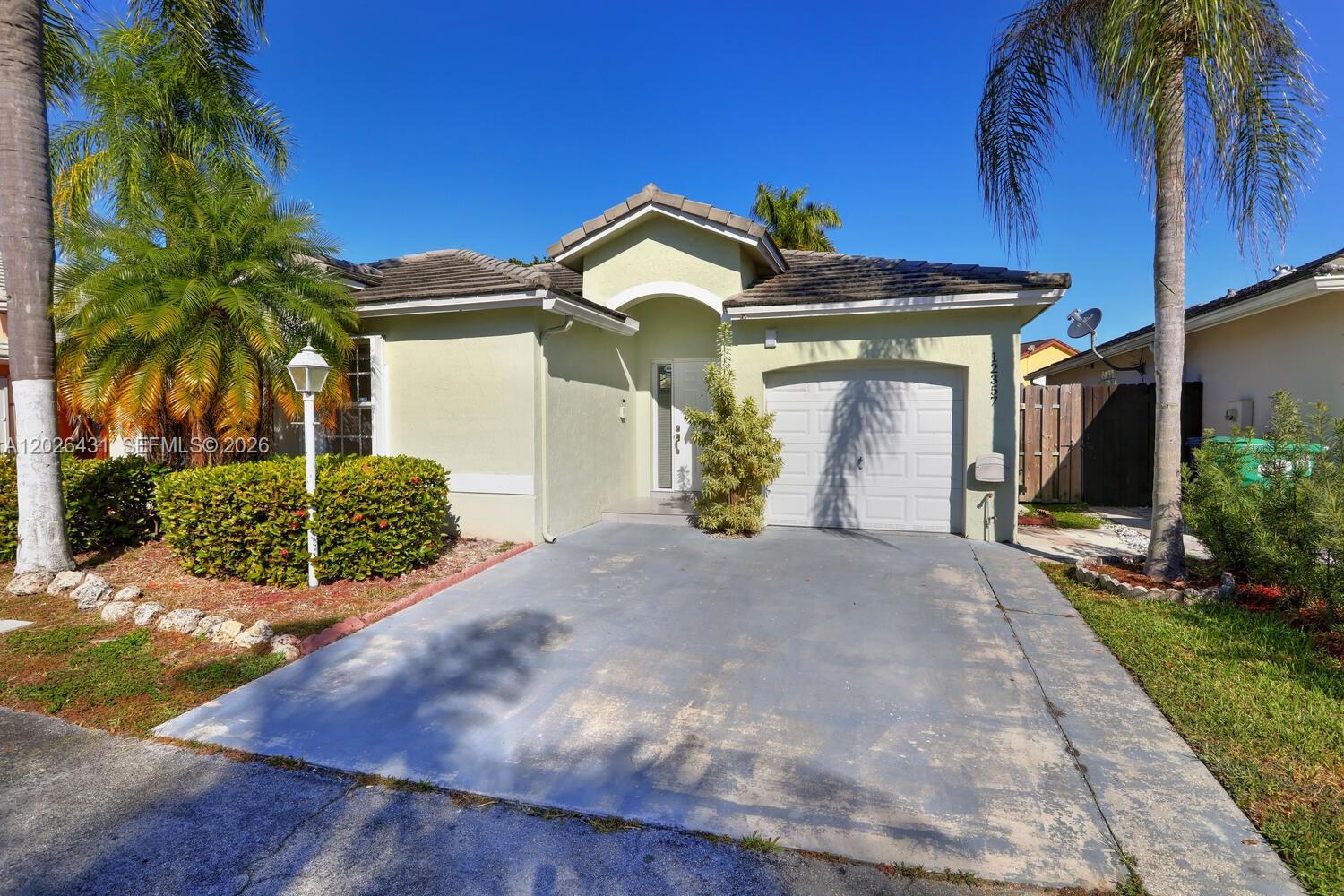 A single-story house features a light green exterior, a one-car garage, and palm trees — 12357 SW 144th Ter, Miami FL 33186, MIAMI, FL
