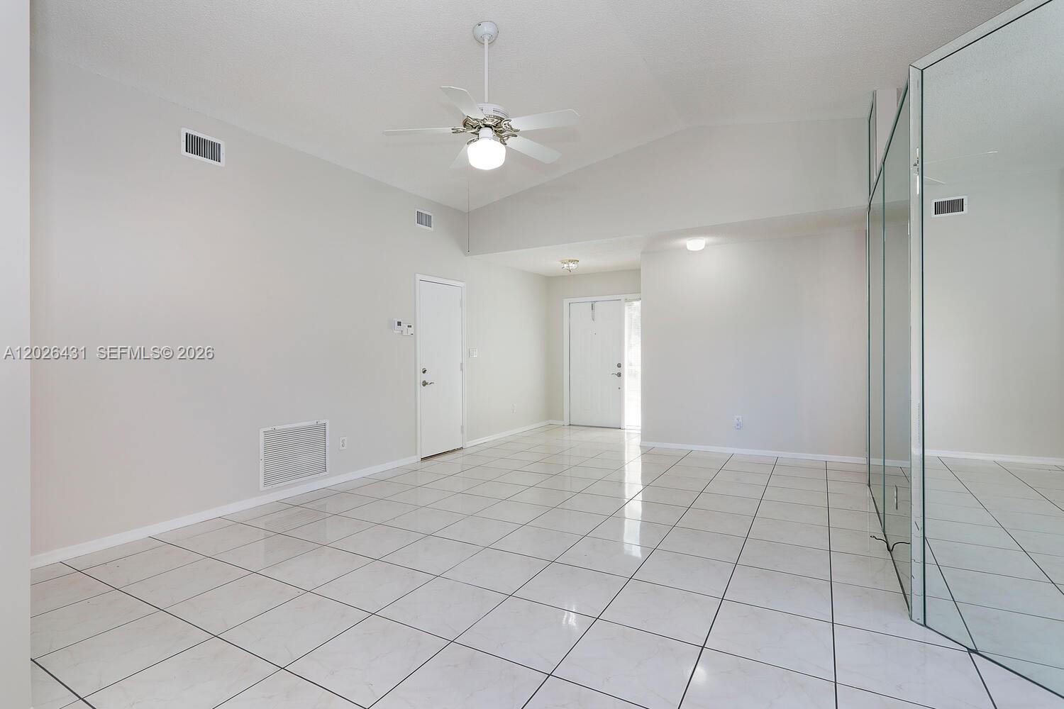 An empty room features white tiled floors, a ceiling fan, and a mirrored wall — 12357 SW 144th Ter, Miami FL 33186, MIAMI, FL