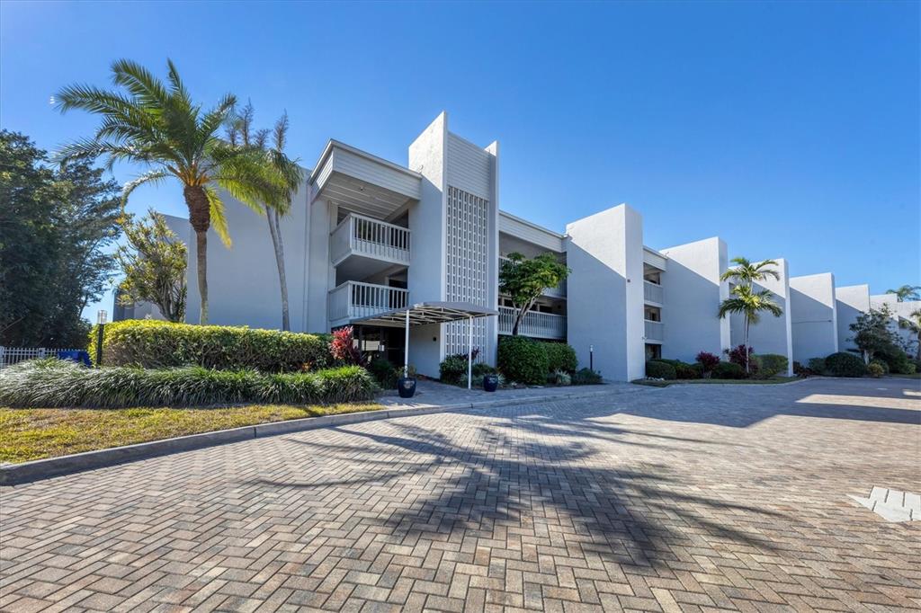 A multi-story apartment building with balconies and palm trees sits behind a paved driveway — 5757 GULF OF MEXICO DRIVE UNIT 305, LONGBOAT KEY, FL