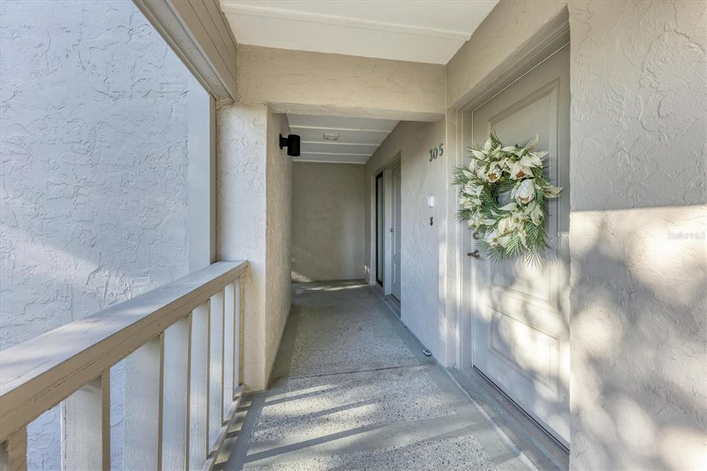 An exterior view of a covered apartment building walkway leading to a front door numbered 305 — 5757 GULF OF MEXICO DRIVE UNIT 305, LONGBOAT KEY, FL