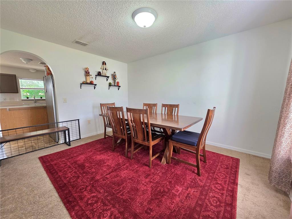 A dining room features a wooden table with six chairs atop a large red rug — 9055 PEMBERTON STREET, SPRING HILL, FL
