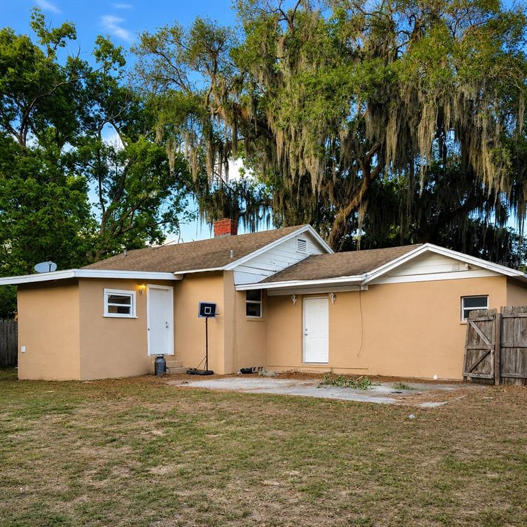 A tan stucco house with blue trim, a concrete driveway, and a brick chimney — 109 N OAKLAND STREET, LEESBURG, FL