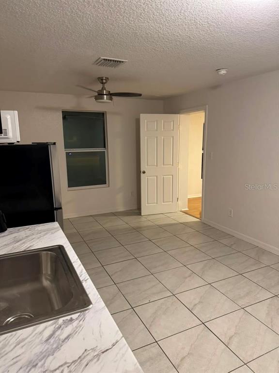 A kitchen with gray cabinets, marble-look backsplash, stainless steel refrigerator, and light tile flooring — 109 N OAKLAND STREET, LEESBURG, FL