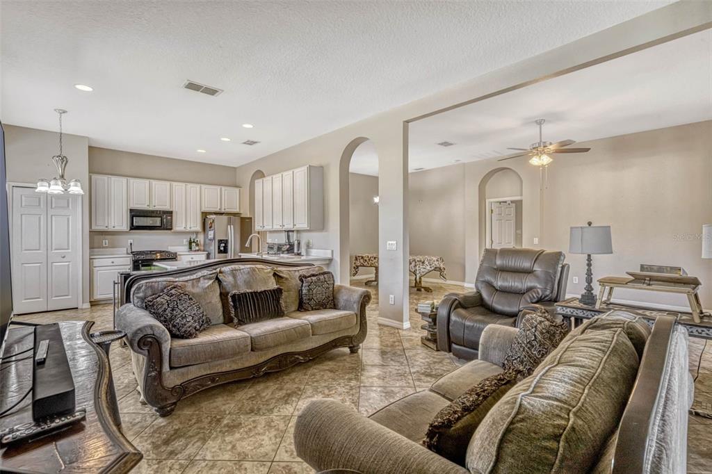 A living room with tile floors opens into a kitchen with white cabinetry and appliances — 115 CRESCENT MOON DRIVE, GROVELAND, FL