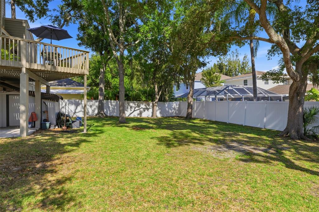 A grassy backyard features a wooden deck, mature trees, and a white vinyl privacy fence — 13150 72ND TERRACE, SEMINOLE, FL