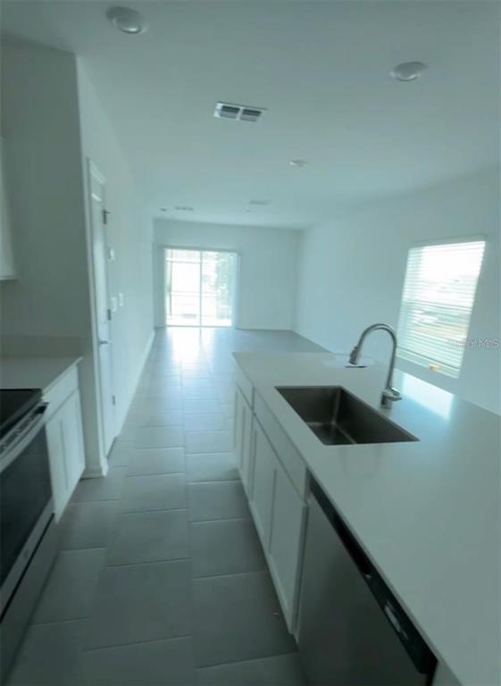 A modern kitchen features white cabinets, a quartz island with a sink, and tile flooring — 2002 PUNCH BOWL AVENUE, DAVENPORT, FL
