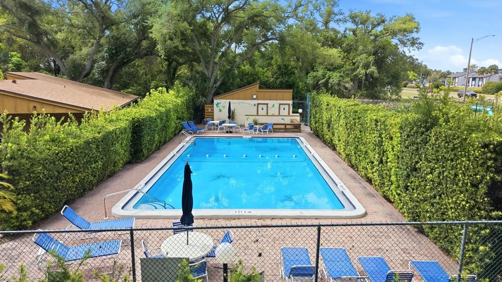 An outdoor swimming pool is surrounded by a brick deck, lounge chairs, and tall hedges — 2510 NIGHTINGALE LANE UNIT 54, BRADENTON, FL
