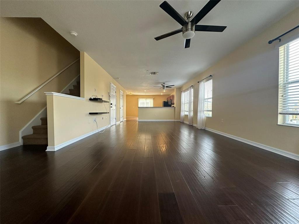 A spacious living area features dark wood flooring, a ceiling fan, and an adjacent staircase — 4405 TUSCAN LOON DRIVE, TAMPA, FL