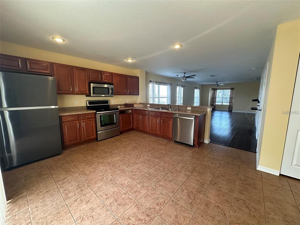 A kitchen with wood cabinets, stainless steel appliances, and tile flooring opens to a living area — 4405 TUSCAN LOON DRIVE, TAMPA, FL