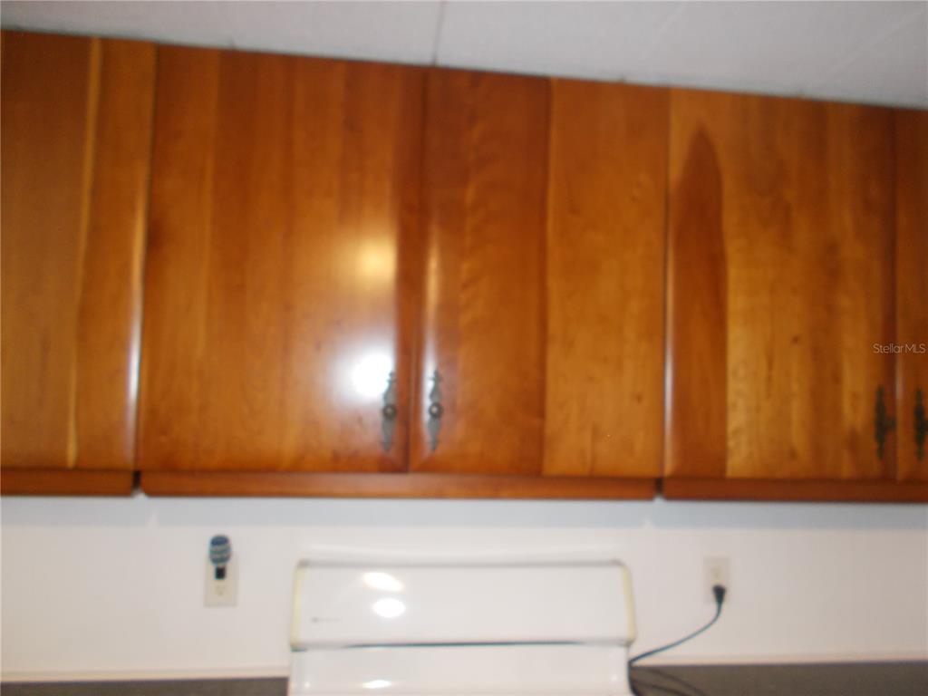 A white stove sits below wooden kitchen cabinets mounted on a white wall — 5039 PALENA BOULEVARD, NORTH PORT, FL