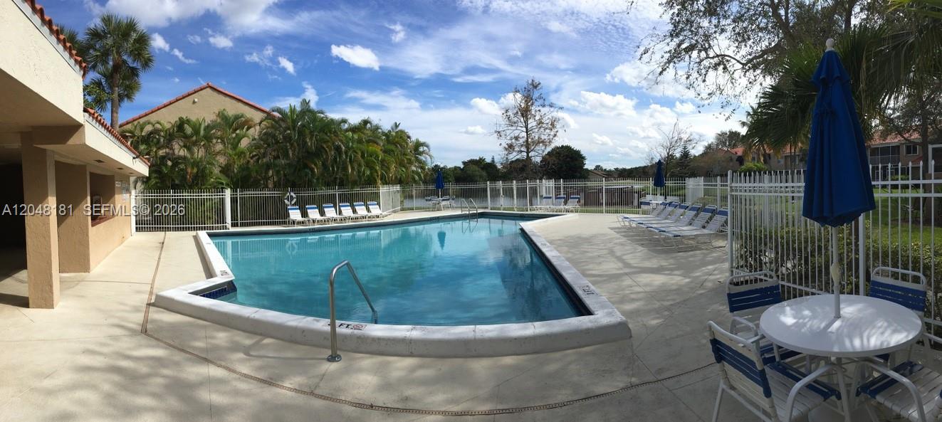 A swimming pool with a surrounding patio, lounge chairs, and a table with an umbrella — 7885 NW 7th Ct # 406, Plantation FL 33324, PLANTATION, FL