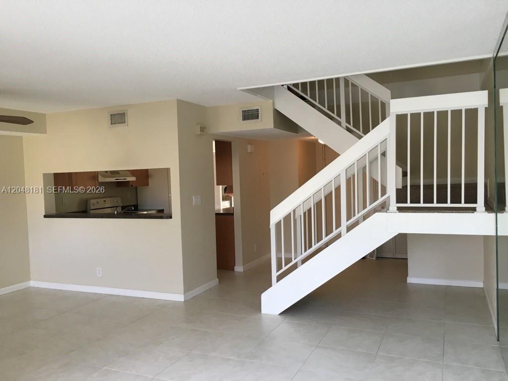 An interior view shows a tiled living area with a staircase and a kitchen pass-through — 7885 NW 7th Ct # 406, Plantation FL 33324, PLANTATION, FL