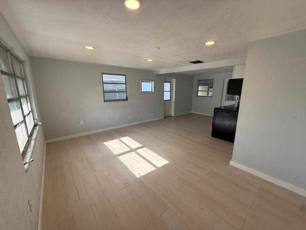 An empty room with light wood-look flooring, recessed lighting, and a black kitchen counter — 1220 12TH AVENUE W, PALMETTO, FL