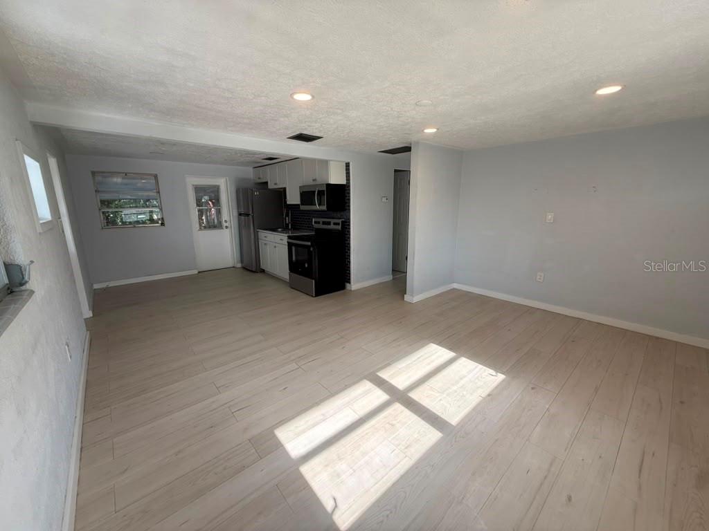An open-concept living area with light wood-look flooring leads into a small kitchen — 1220 12TH AVENUE W, PALMETTO, FL