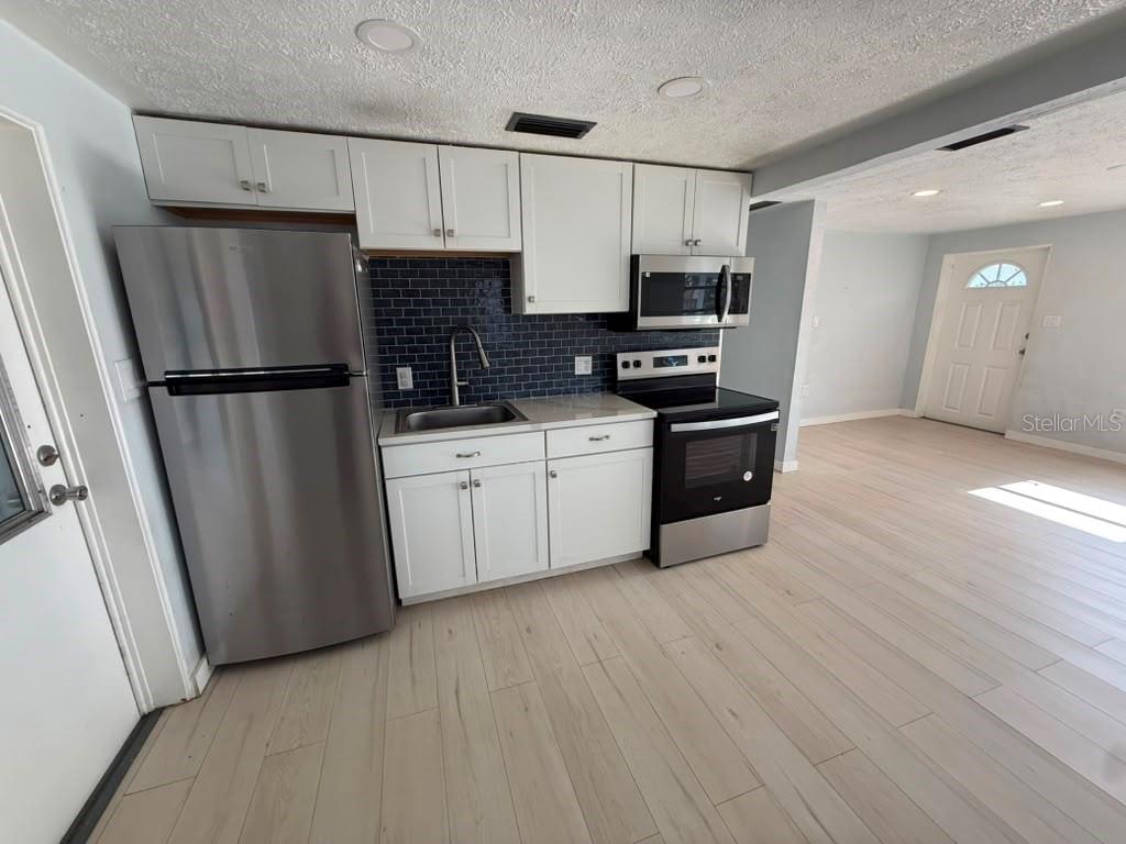 A kitchen features white cabinets, stainless steel appliances, and a dark blue subway tile backsplash — 1220 12TH AVENUE W, PALMETTO, FL