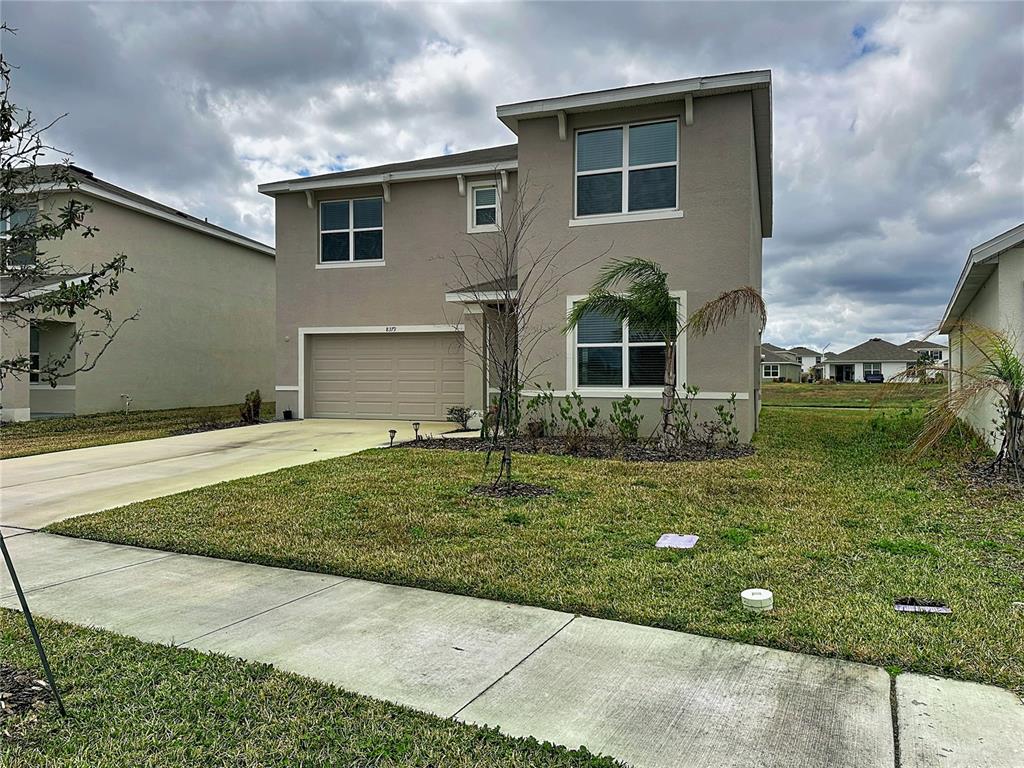 A two-story suburban house with a tan stucco exterior, a two-car garage, and a lawn — 8379 ENDER HILLS DRIVE, WESLEY CHAPEL, FL
