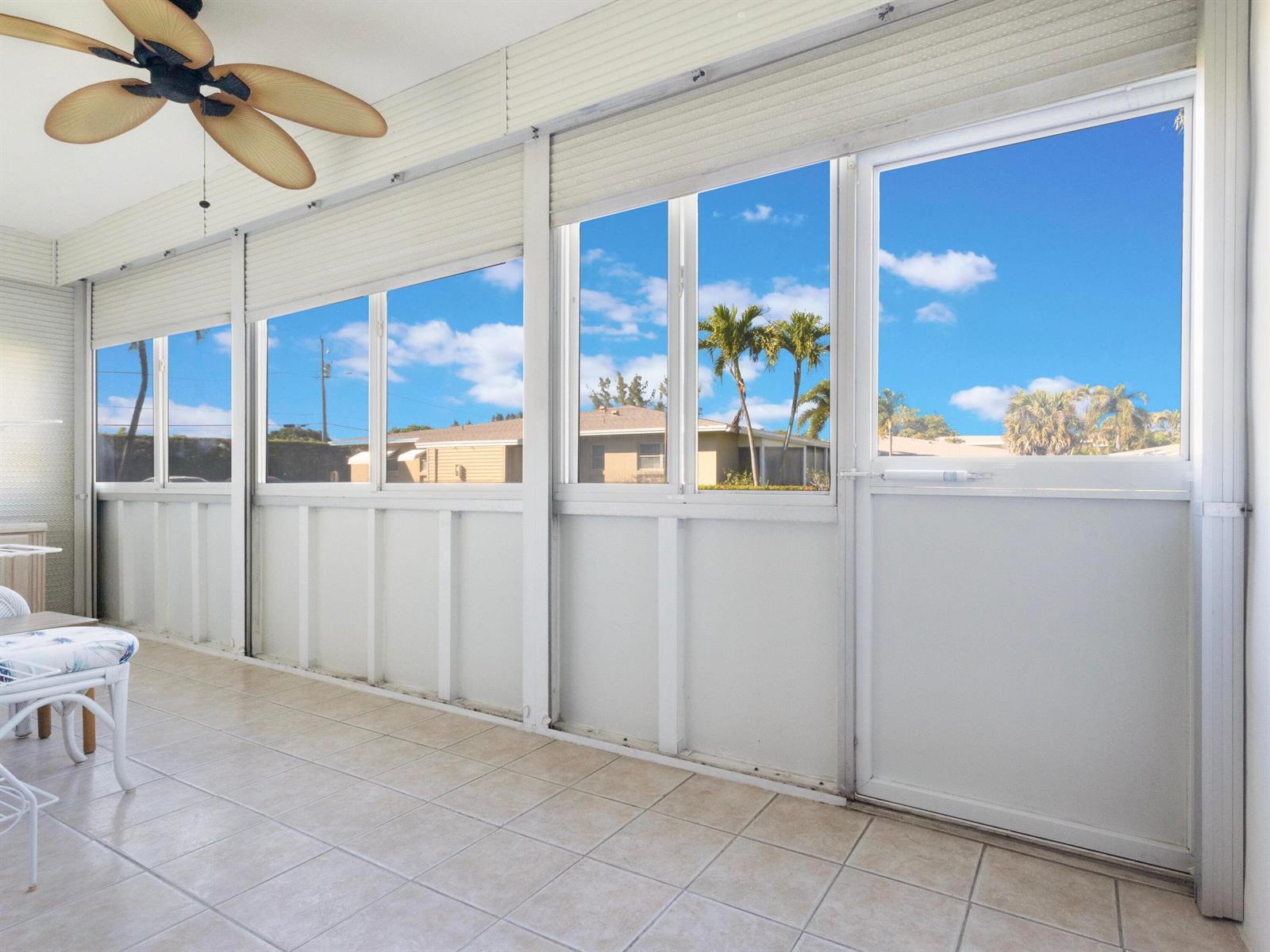 A sunroom with tiled floors, a ceiling fan, and large windows overlooking a residential neighborhood — 301 Circle Drive S # 103, Boynton Beach FL 33435, BOYNTON BEACH, FL
