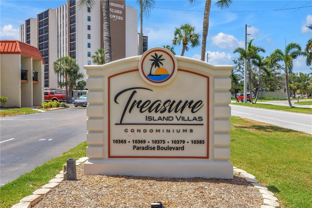 A monument sign for Treasure Island Villas stands in front of a multi-story apartment building — 10365 PARADISE BOULEVARD UNIT 27, ST PETERSBURG, FL