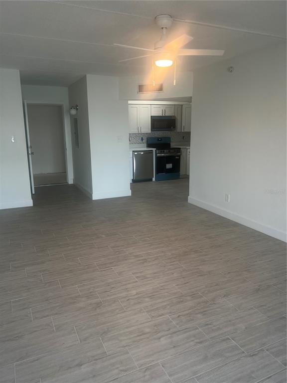 An open-concept living area with light wood-look tile flooring leads into a kitchen with appliances — 10365 PARADISE BOULEVARD UNIT 27, ST PETERSBURG, FL