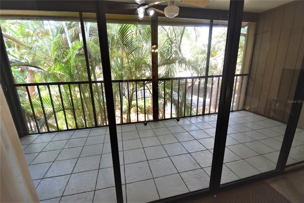 A screened-in balcony features light-colored square floor tiles and a view of palm trees — 1712 GLENHOUSE DRIVE UNIT GL418, SARASOTA, FL