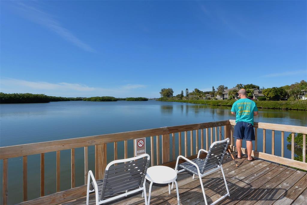 A man fishes from a wooden deck overlooking a calm bay with mangrove shorelines — 1712 GLENHOUSE DRIVE UNIT GL418, SARASOTA, FL