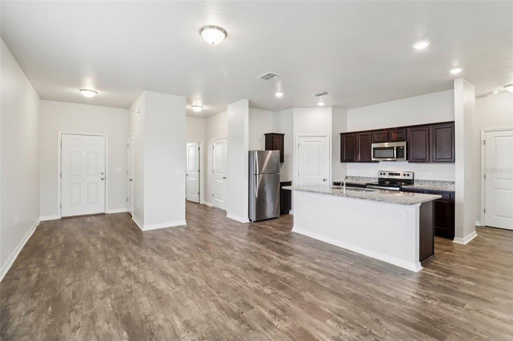 An open-concept kitchen and living area feature dark wood cabinets, stainless steel appliances, and flooring — 3098 NEVERLAND DRIVE, NEW SMYRNA BEACH, FL