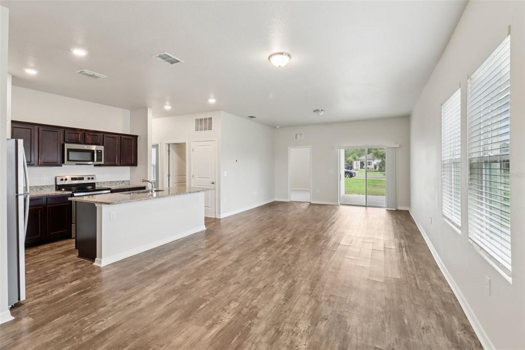 An open-concept kitchen and living area featuring dark wood cabinets, granite countertops, and wood flooring — 3098 NEVERLAND DRIVE, NEW SMYRNA BEACH, FL