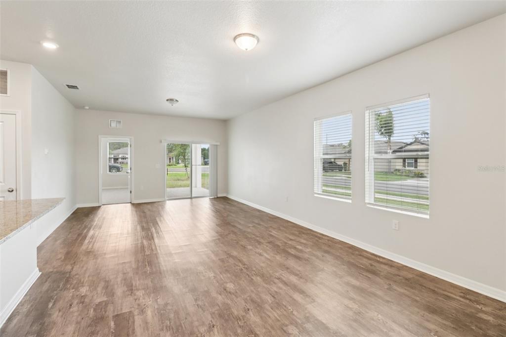 An empty living room features light wood-look flooring, white walls, and two large windows — 3098 NEVERLAND DRIVE, NEW SMYRNA BEACH, FL