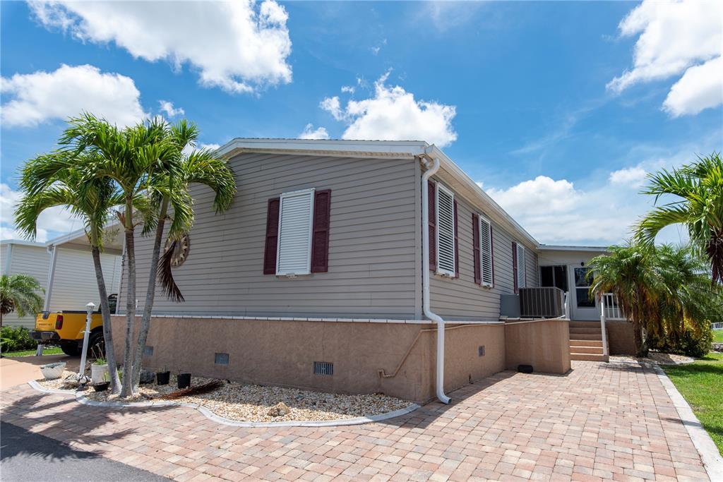 A single-story manufactured home with grey siding, maroon shutters, and a paved brick driveway — 53 ROTTERDAM DRIVE, PUNTA GORDA, FL