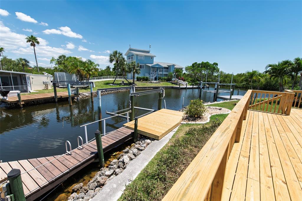 A wooden deck overlooks a canal with a boat dock and a multi-story blue house — 53 ROTTERDAM DRIVE, PUNTA GORDA, FL