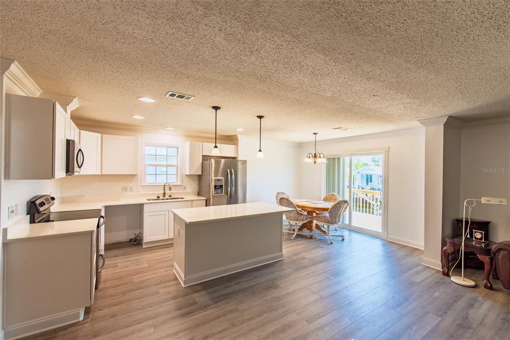 A kitchen with white cabinets, a center island, and wood-look flooring opens to a dining area — 53 ROTTERDAM DRIVE, PUNTA GORDA, FL