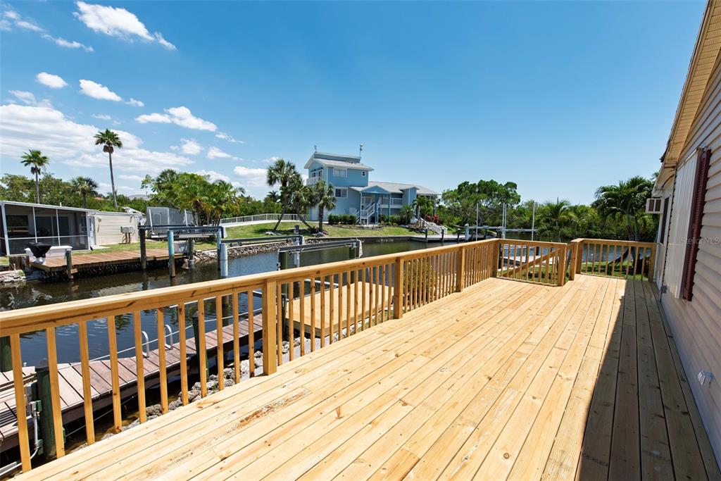 A wooden deck overlooks a canal with a dock and a blue house in the distance — 53 ROTTERDAM DRIVE, PUNTA GORDA, FL