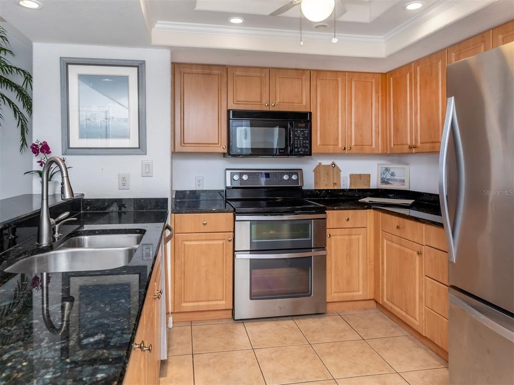 A kitchen with light wood cabinets, black granite countertops, and stainless steel appliances — 601 SHREVE STREET UNIT 51B, PUNTA GORDA, FL
