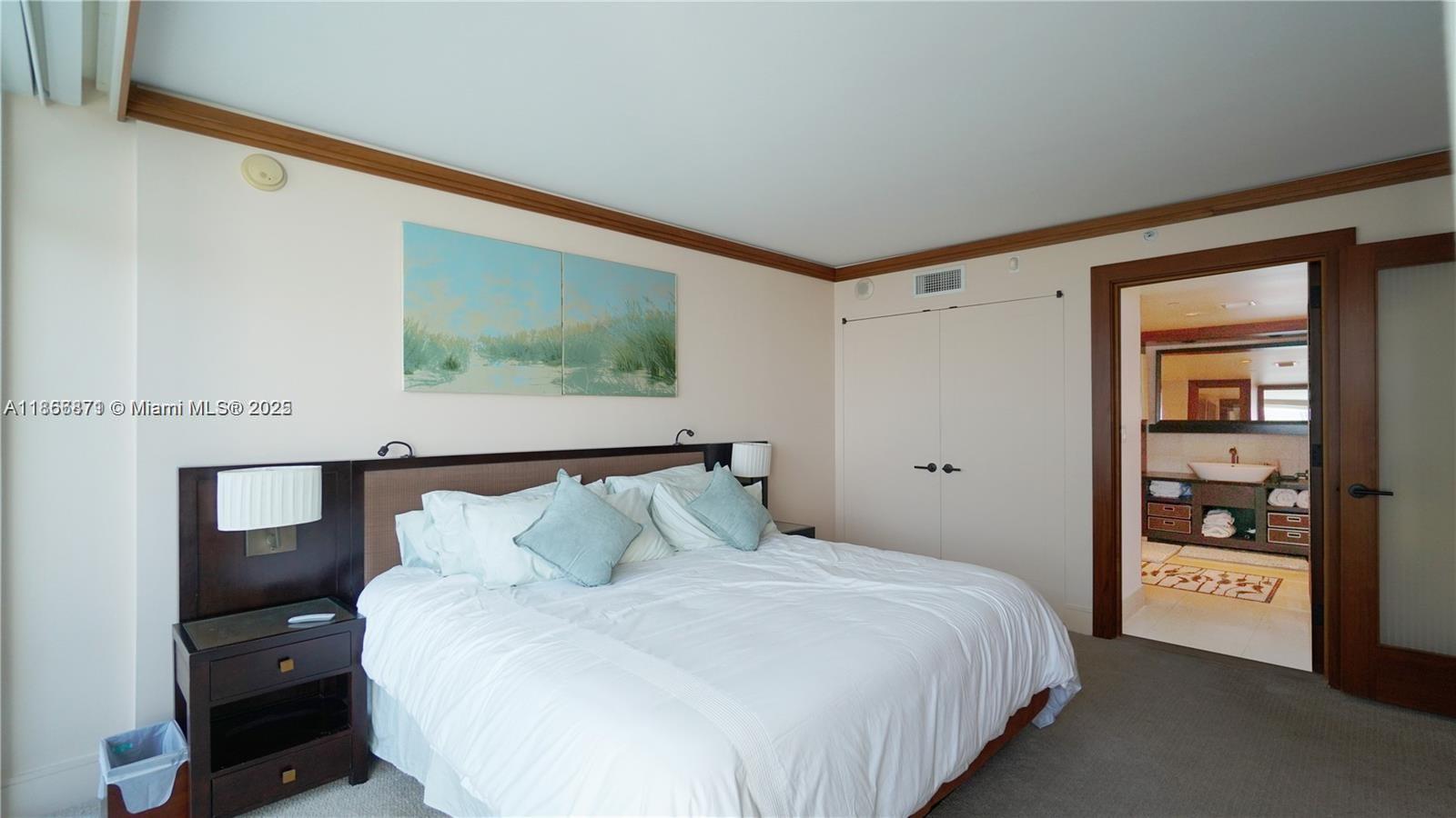 A bedroom features a king bed, dark wood headboard, nightstands, and an attached bathroom — 6801 Collins Ave # 710, Miami Beach FL 33141, MIAMI BEACH, FL