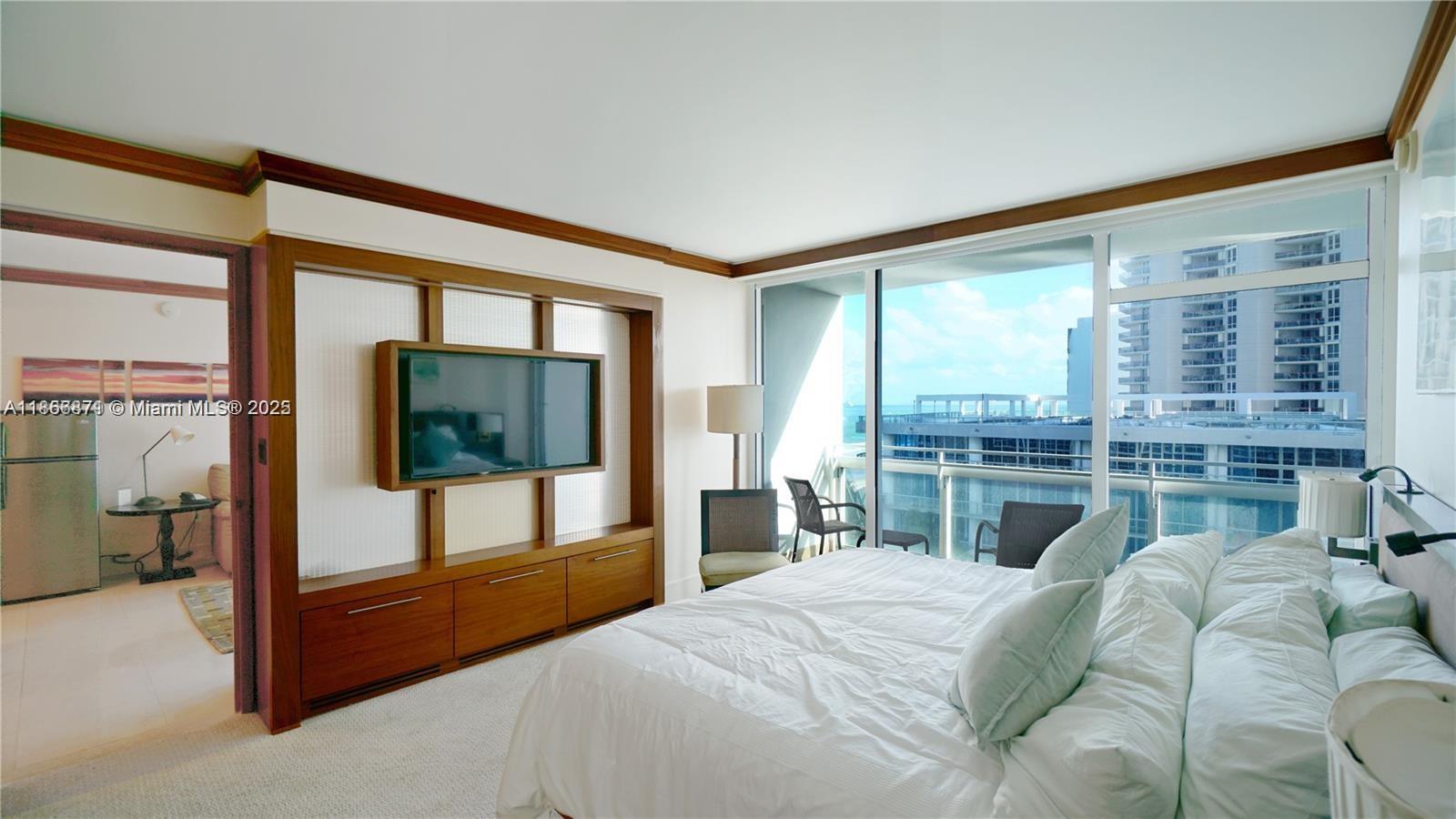 A bedroom features a wall-mounted television, wooden cabinetry, and a balcony overlooking the ocean — 6801 Collins Ave # 710, Miami Beach FL 33141, MIAMI BEACH, FL