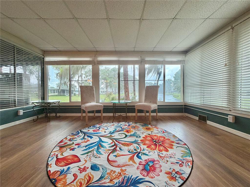 A sunroom features wood-look flooring, a floral area rug, two chairs, and large windows — 320 PALO VERDE DRIVE, LEESBURG, FL