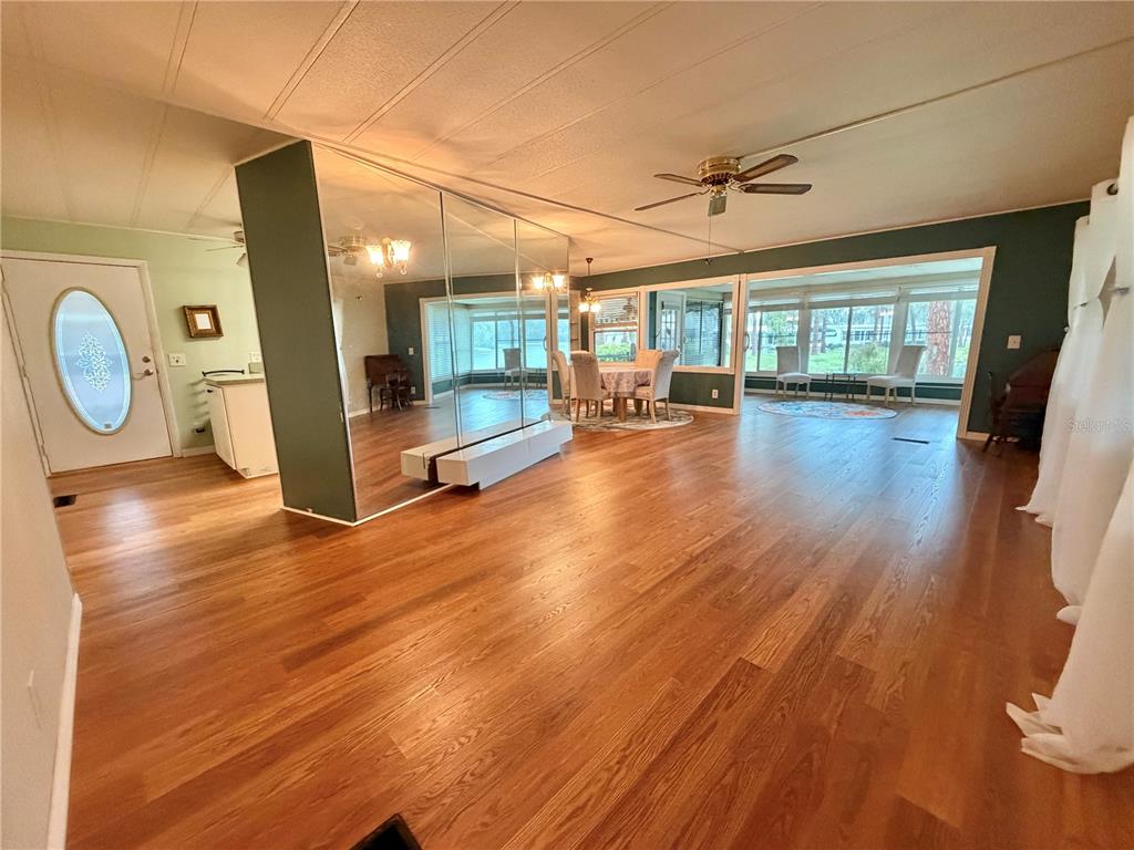 A living room with wood flooring, a mirrored wall, and a view into a sunroom — 320 PALO VERDE DRIVE, LEESBURG, FL