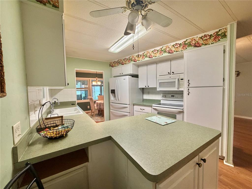 A kitchen features green countertops, white cabinetry, a ceiling fan, and a view into another room — 320 PALO VERDE DRIVE, LEESBURG, FL