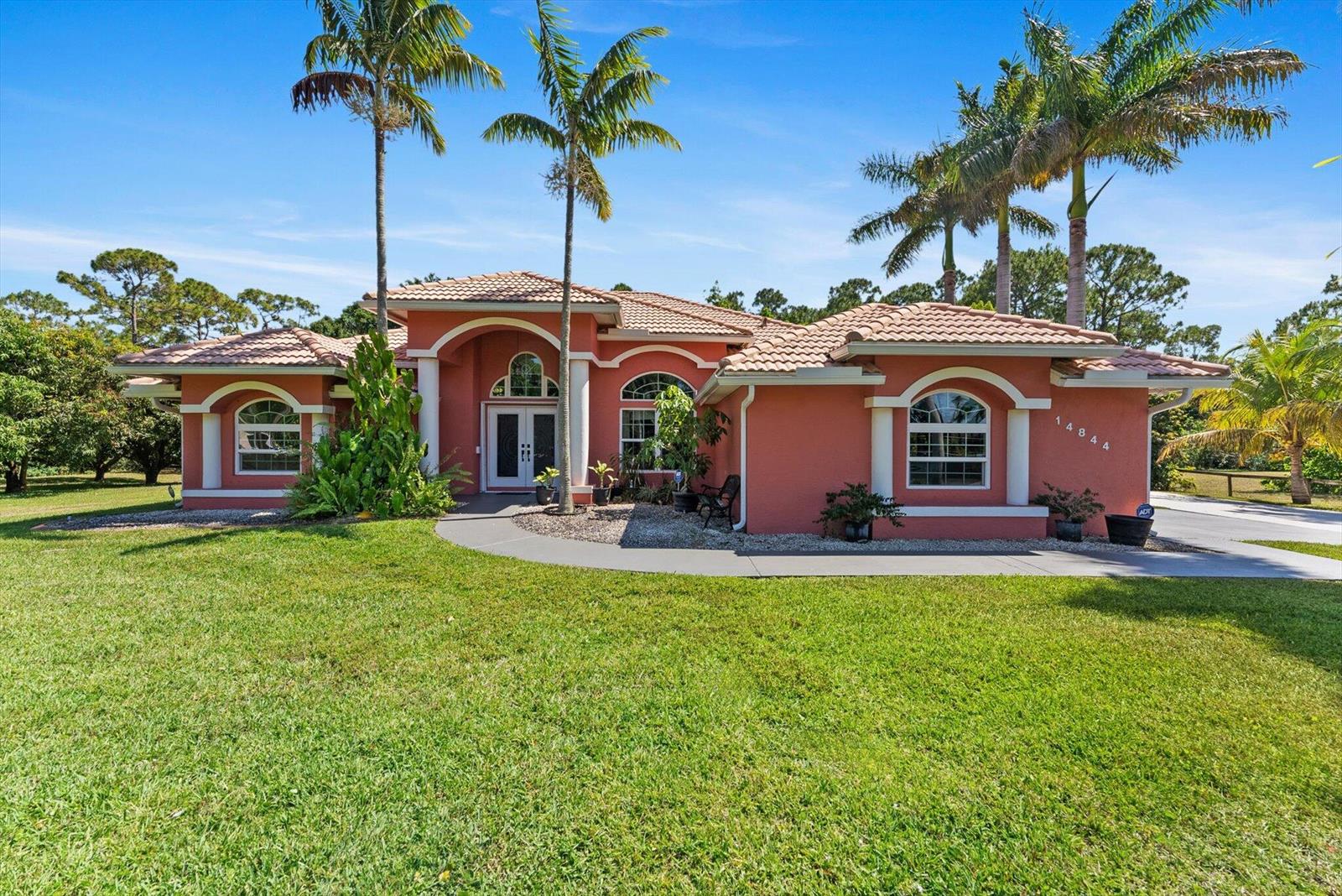 A single-story peach-colored house with a tile roof and palm trees in the front yard — 14844 Tangerine Boulevard, FL 33470, FL