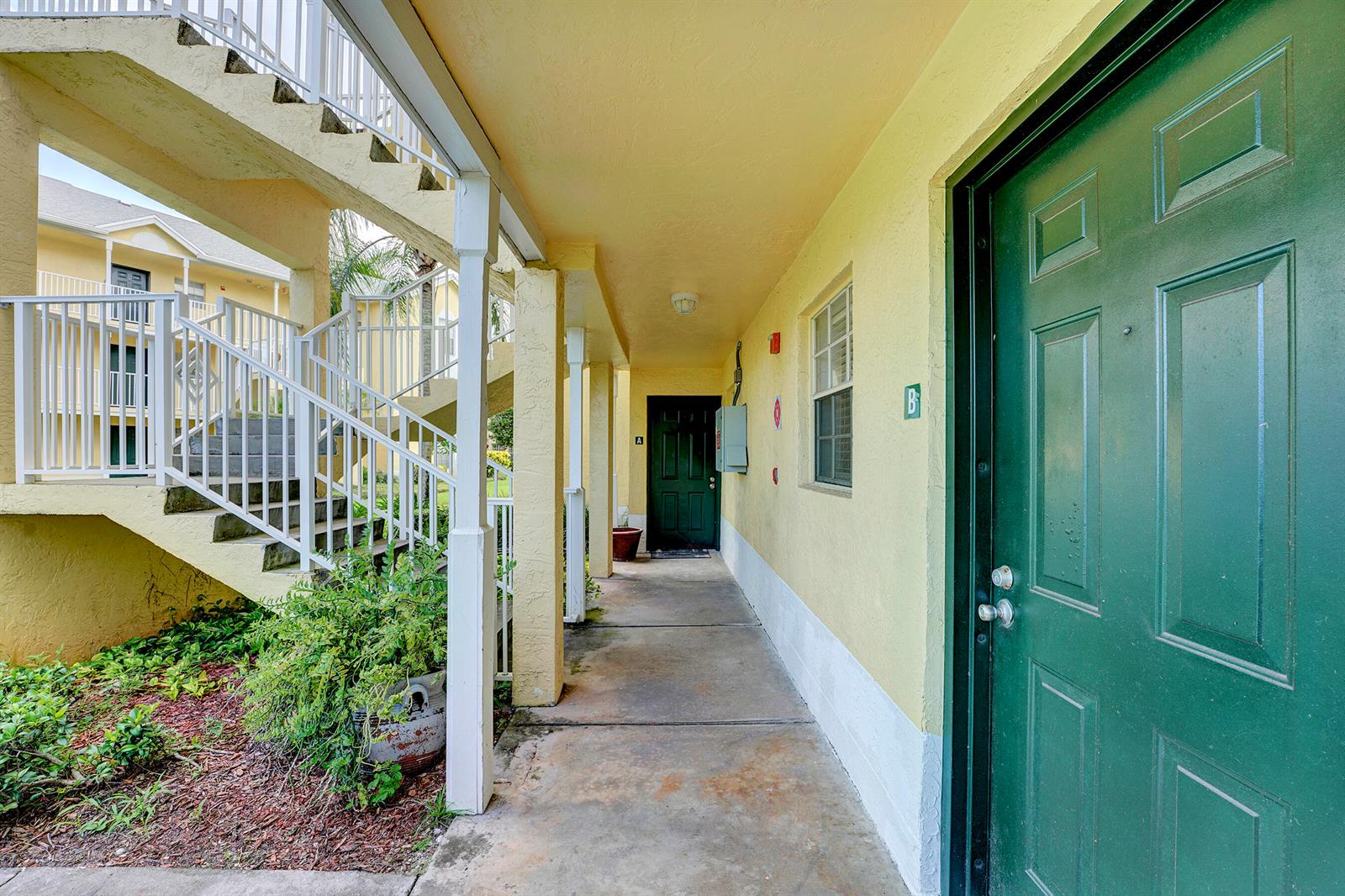 A walkway with yellow walls leads to two green doors under a covered exterior corridor — 6315 La Costa Drive # A, Boca Raton FL 33433, BOCA RATON, FL