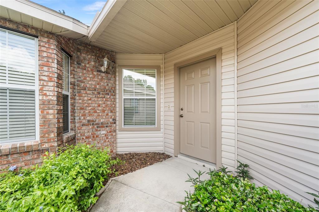 A beige front door is set into a house exterior with brick and vinyl siding — 4912 NW 79TH ROAD, GAINESVILLE, FL