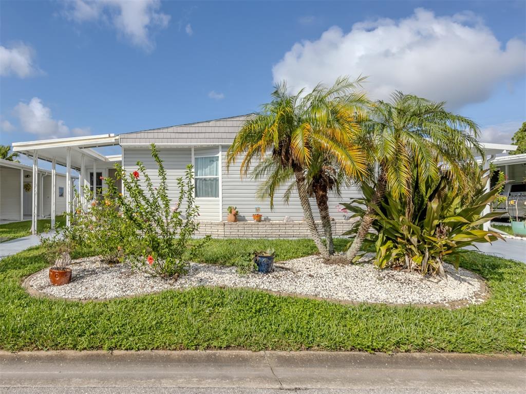 A single-story manufactured home features light gray siding, a covered carport, and landscaped front yard — 97 LAKEVIEW DRIVE, NORTH PORT, FL
