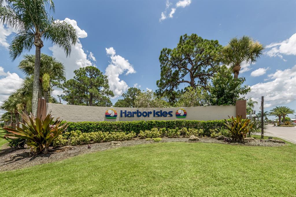 A beige stucco entrance sign for Harbor Isles sits in a landscaped lawn with palm trees — 97 LAKEVIEW DRIVE, NORTH PORT, FL