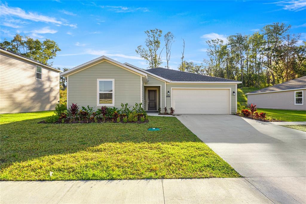 A single-story house with light green siding, a two-car garage, and a front lawn — 16983 NW 144TH STREET, ALACHUA, FL
